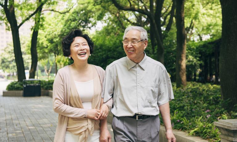 Cheerful senior Chinese couple spending a sunny spring day talking and walking through a park