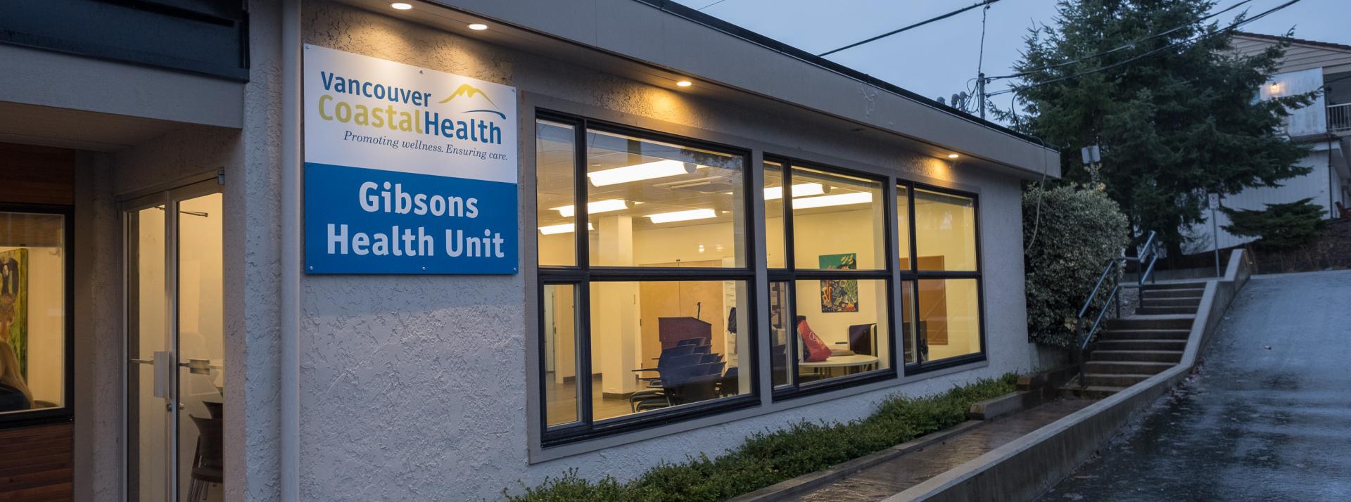 Exterior shot of Gibsons Health Unit at dusk.  The lights are on inside and the sign is visible on the outside.