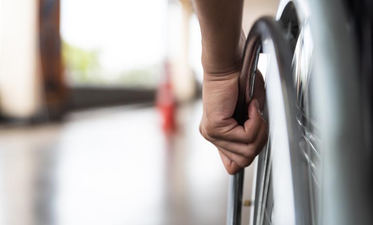 Close up of a persons hand on a wheelchair wheel in a hallway