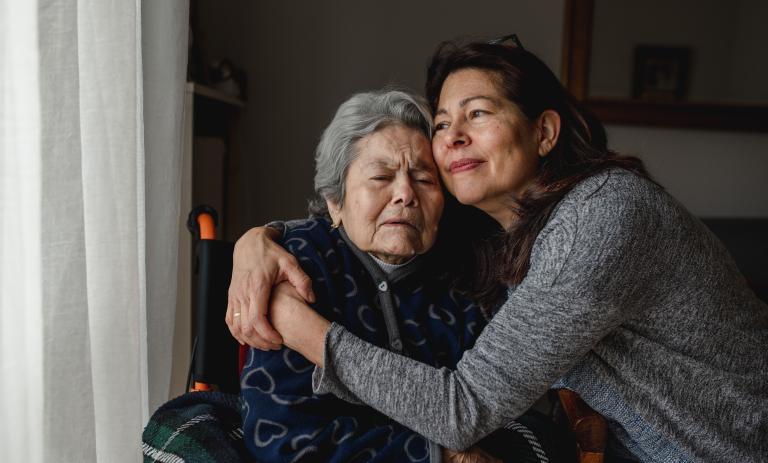 Caregiver hugging elderly woman in a wheelchair