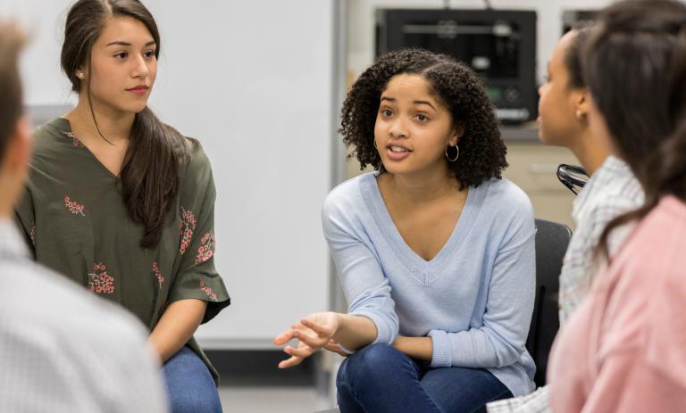Girl gestures while talking with fellow teenagers during a support group meeting.