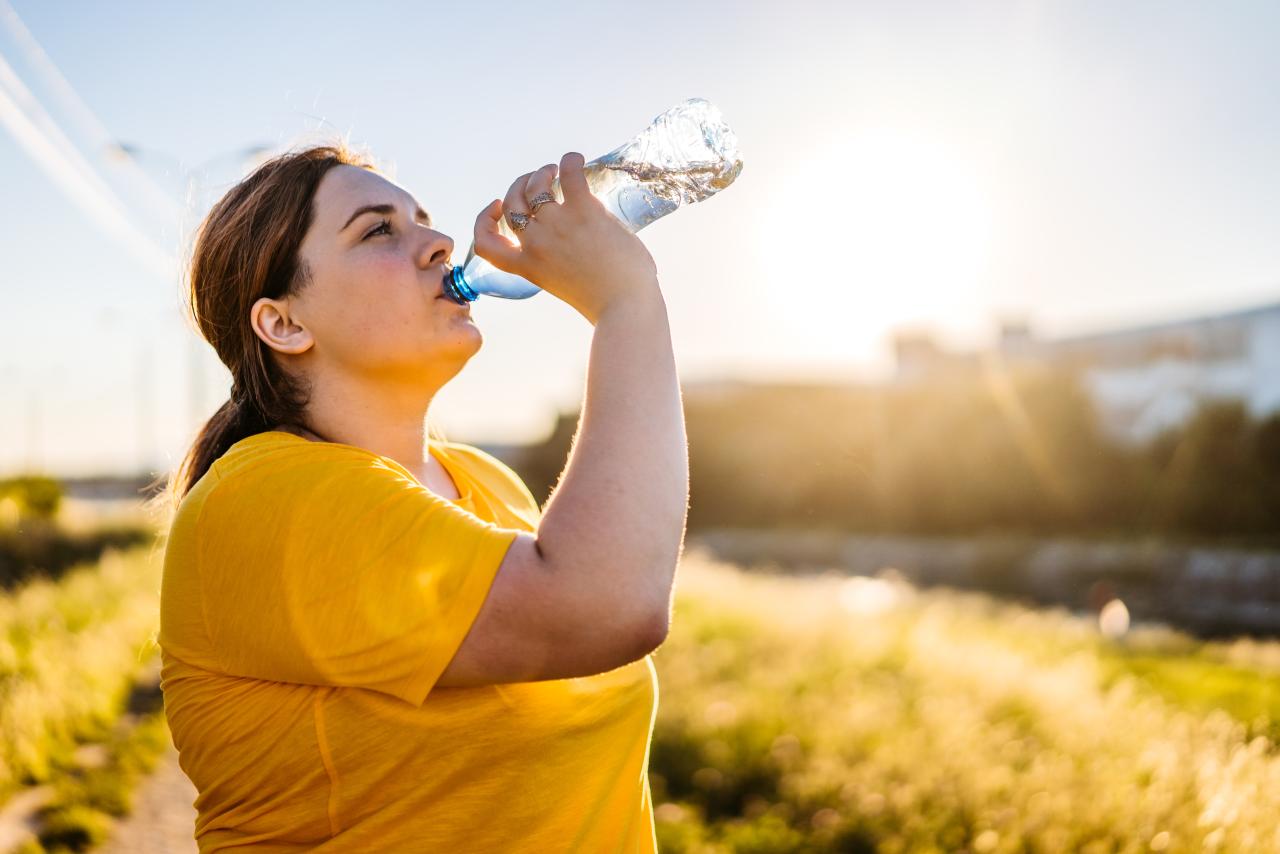 person drinking water on a sunny day after running in a public park