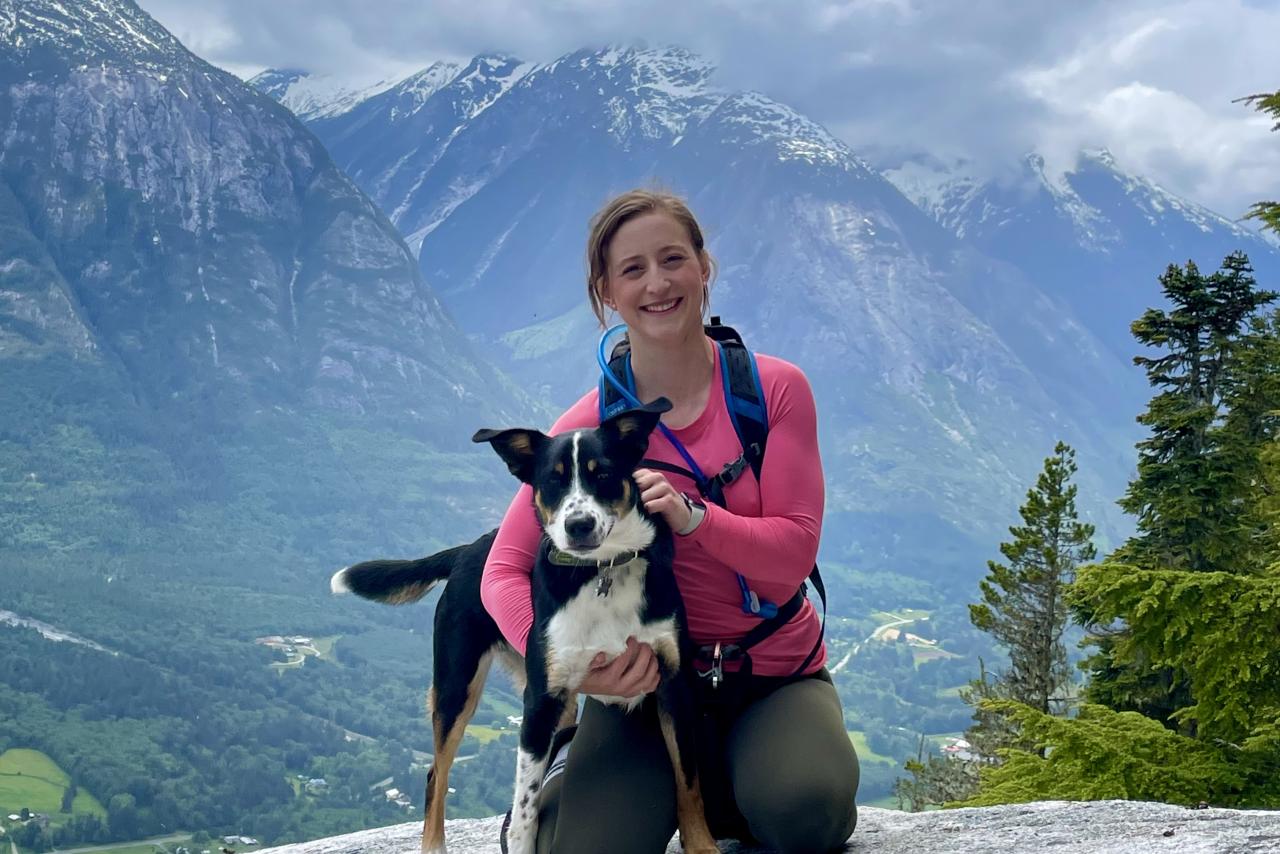 Brooke Meunier, LPN, crouched on a cliff with a dog in arm.