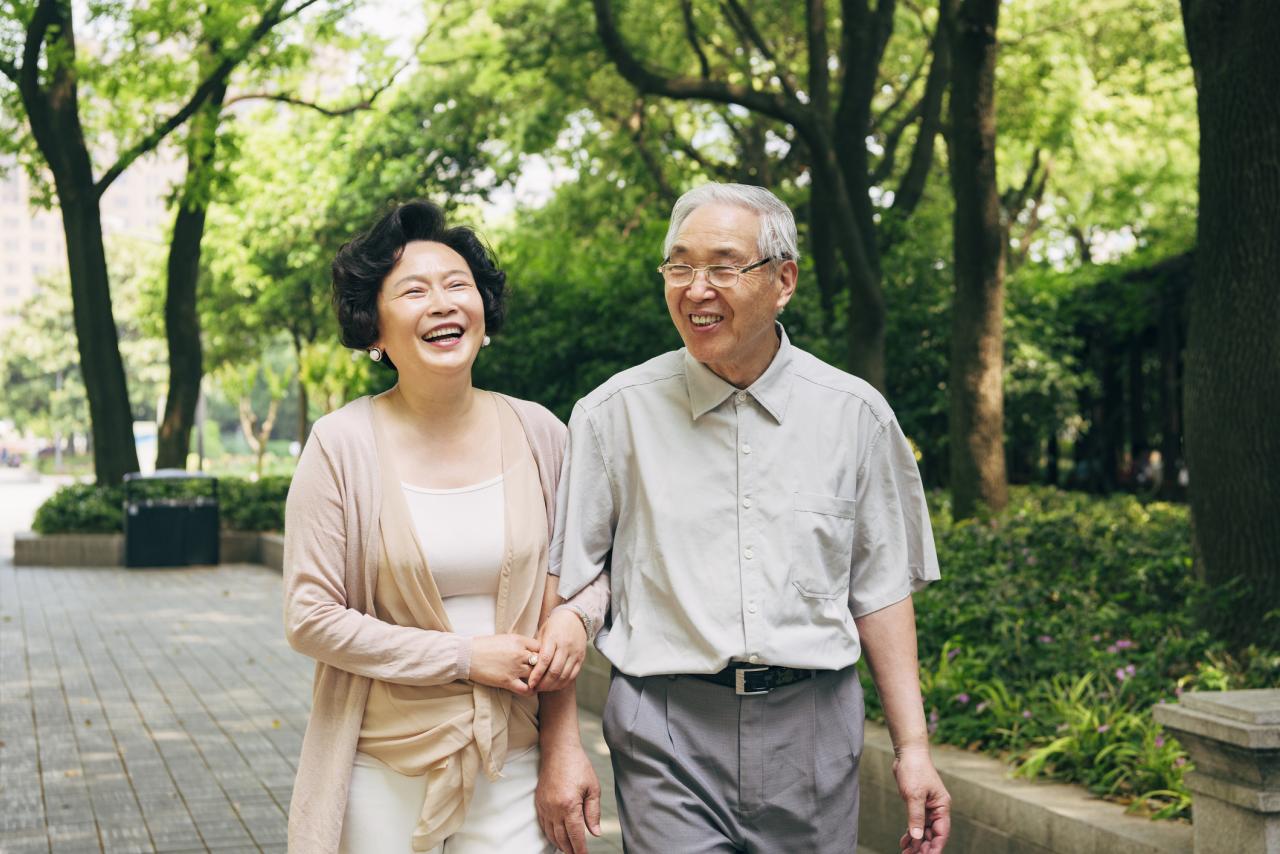 Cheerful senior Chinese couple spending a sunny spring day talking and walking through a park