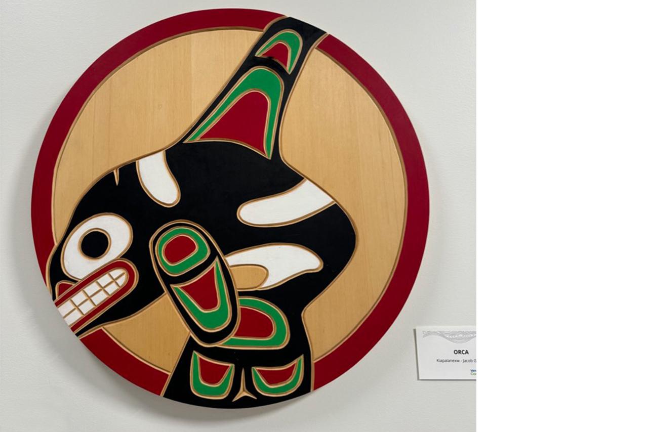 Indigenous wooden carving of an orca mounted on a white wall 