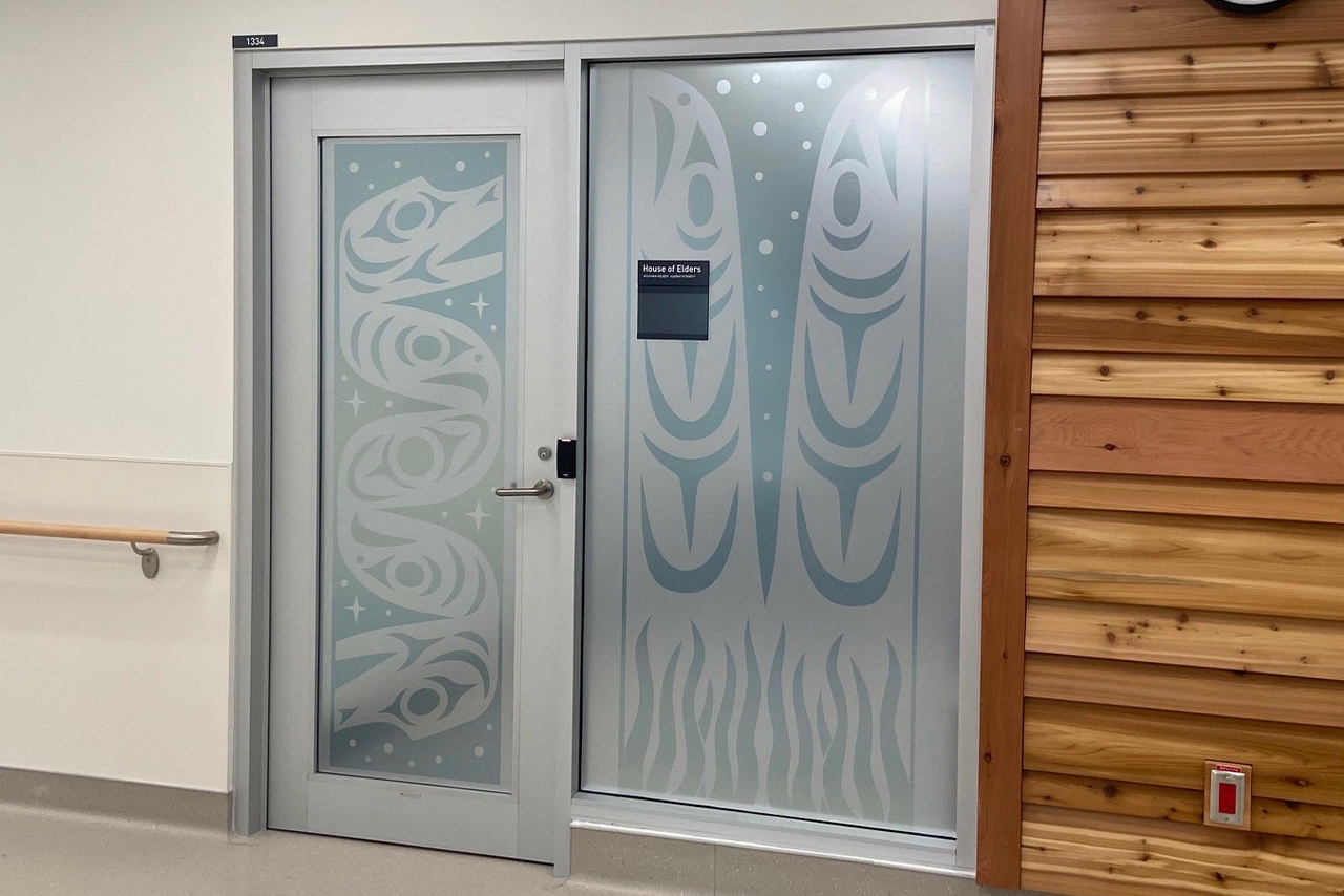 Indigenous artwork of a serpent, salmon and eelgrass mural on top of windows and a door