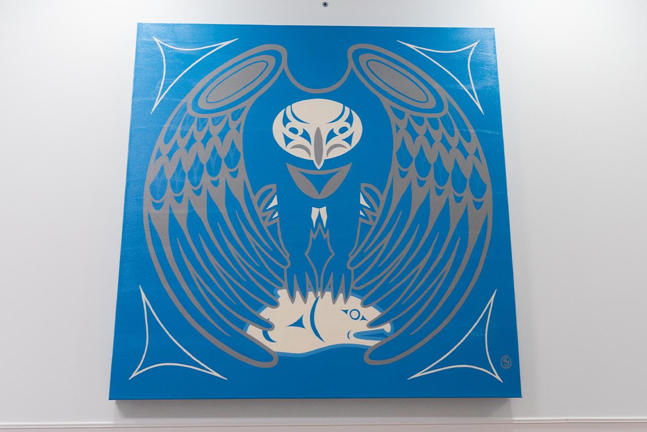 Indigenous artwork in blue of an eagle mounted on a white wall 