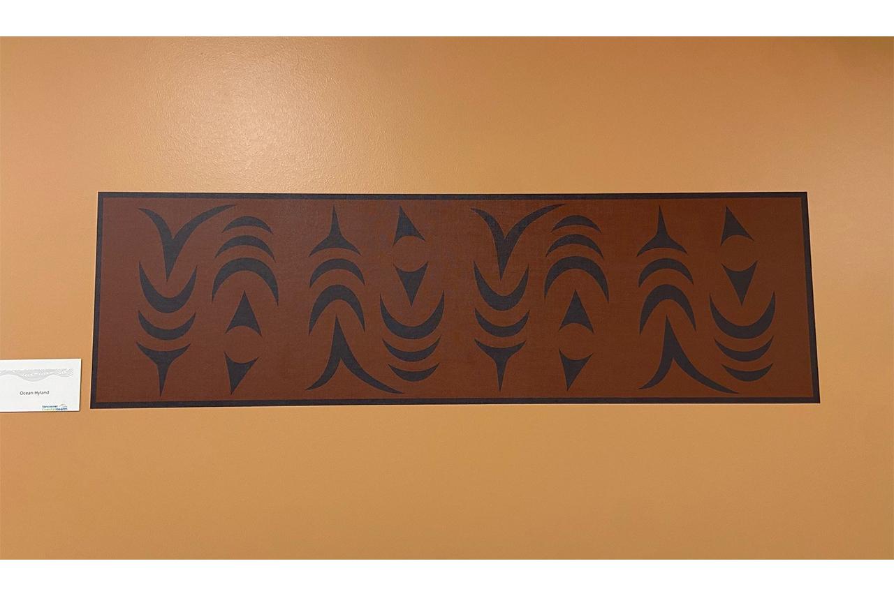 Indigenous artwork in an ochre colour of salmon mounted on a white wall 