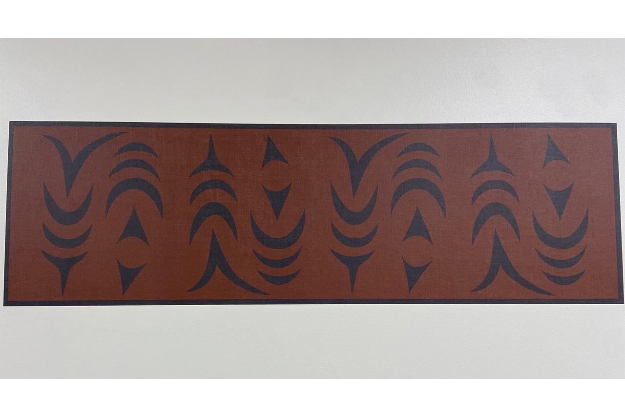 Indigenous artwork in an ochre colour of salmon mounted on a white wall 