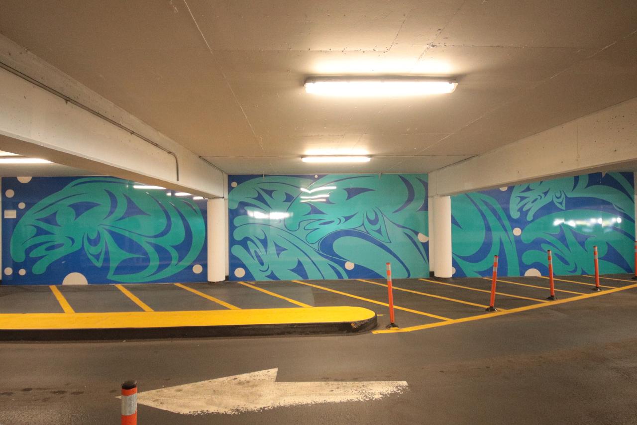Indigenous mural on the walls inside a parkage in dark blue and teal of a school of salmon