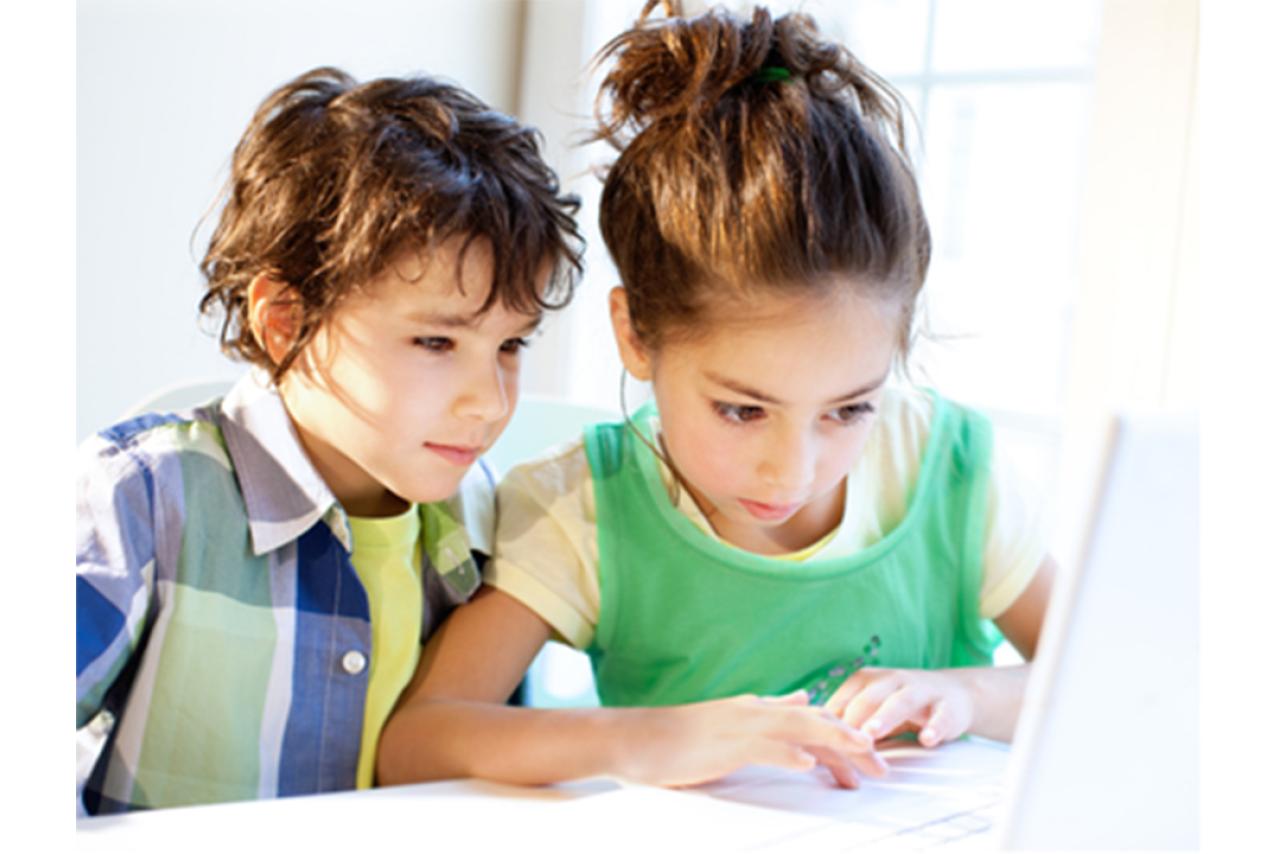A young boy and girl who have brown hair sitting and looking at a laptop screen
