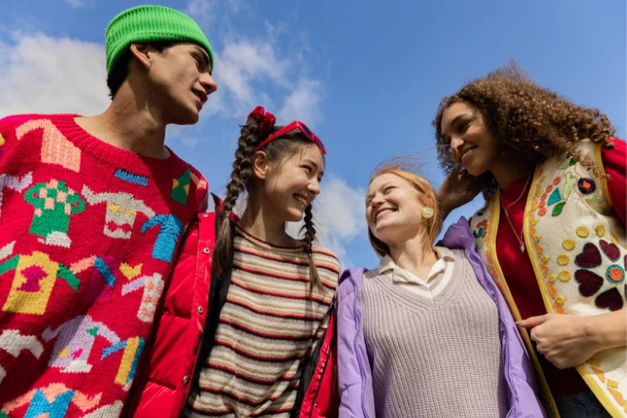 A group of four diverse youth smiling with the blue sky in the background