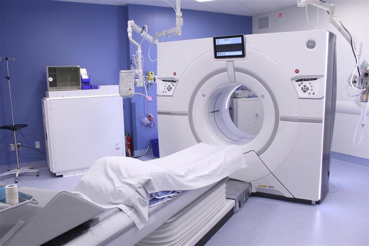 A white CT scanner in a medical exam room with soft blue walls