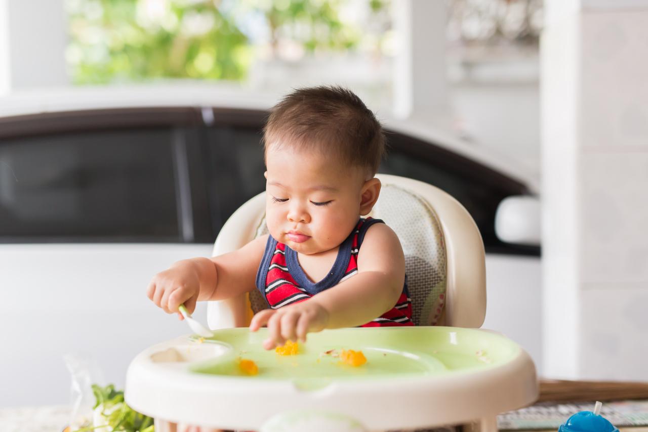 A toddler in a high chair   eating food with their fingers.