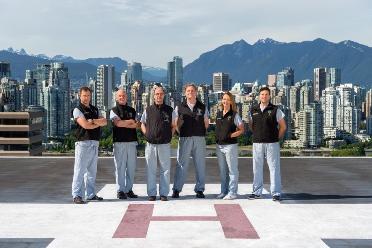 Six members of a trauma team stand on a helipad with mountains in the background.