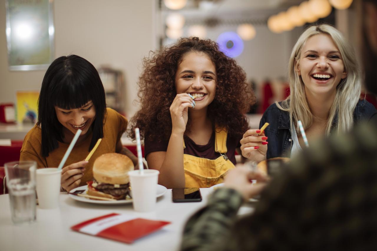 Three teenagers smiling and eating french fries at a restaurant.
