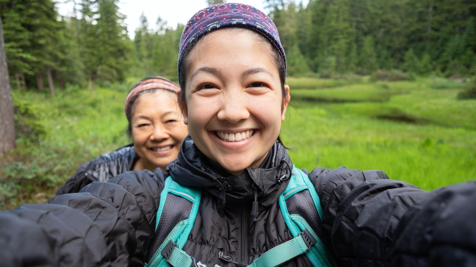Two people standing in a forested area with smiling faces.