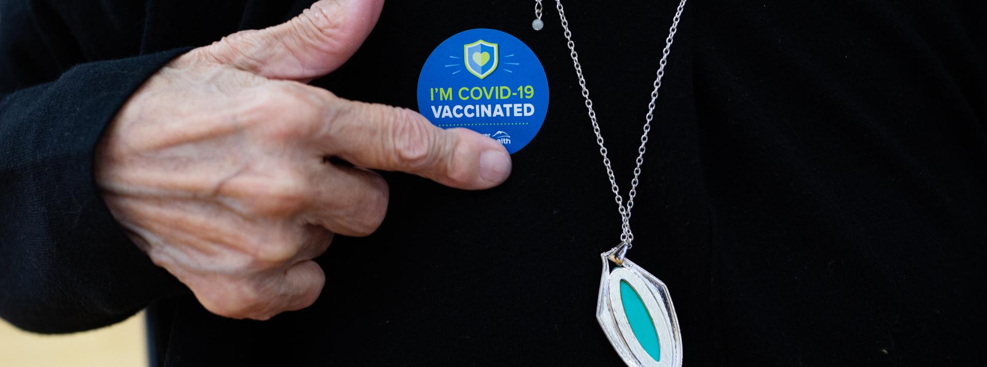 person pointing to COVID-19 vaccine sticker