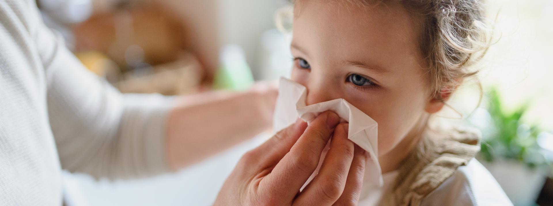 A parent blowing nose of small sick daughter indoors at home