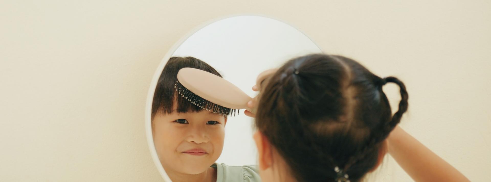 A child brushing their hair in the mirror.