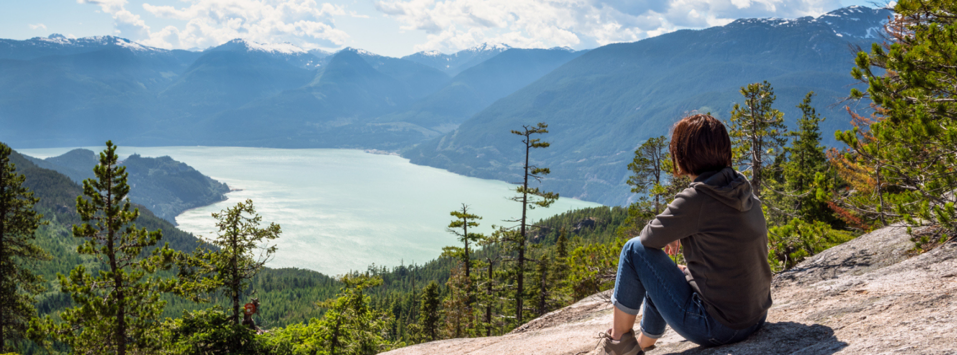 Person sitting on mountain in Squamish looking out at view of mountains and water below.