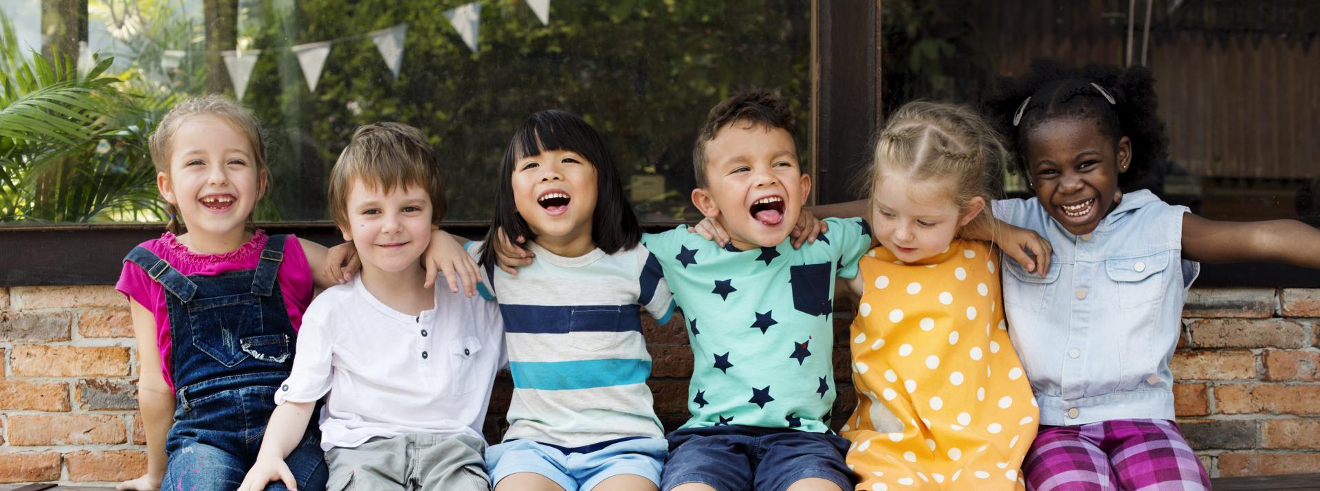A group photo of six children laughing outside.
