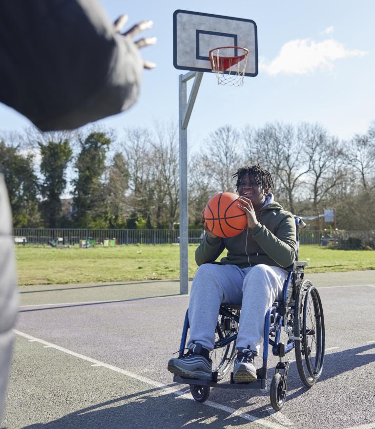 A teenager in a wheelchair playing basketball with friends at the park
