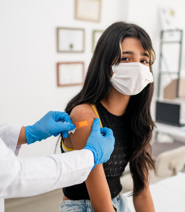 A school aged girl getting a bandaid on her arm after a routine immunization
