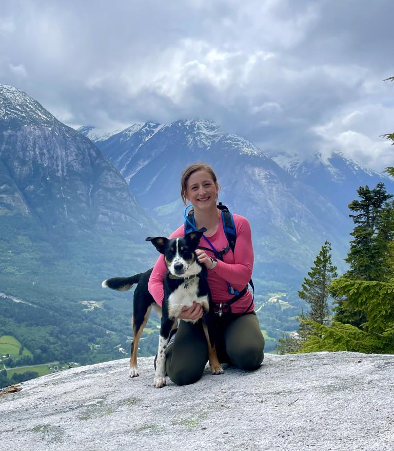 Brooke Meunier, LPN, crouched on a cliff with a dog in arm.