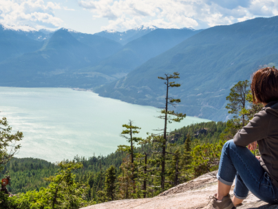 Person sitting on mountain in Squamish looking out at view of mountains and water below.