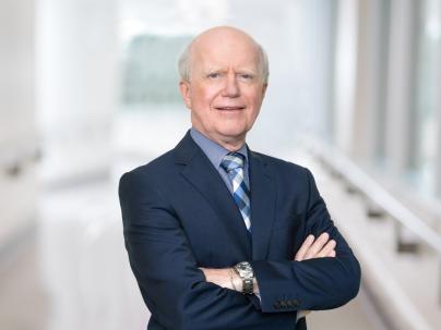 A portrait for Dr. Gavin Stuart in a brightly lit white hallway. He is wearing a dark blue blazer.