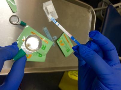 Two gloved hands using a fentanyl test strip to test a drug sample
