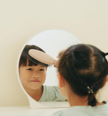 A child brushing their hair in the mirror.
