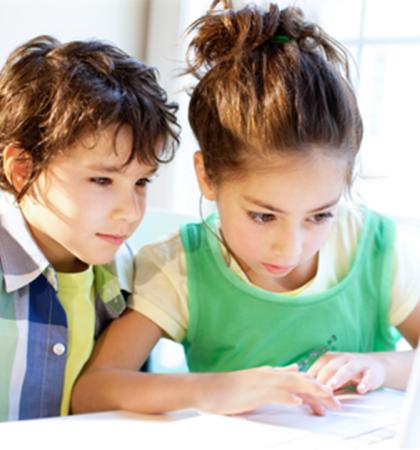 A young boy and girl who have brown hair sitting and looking at a laptop screen